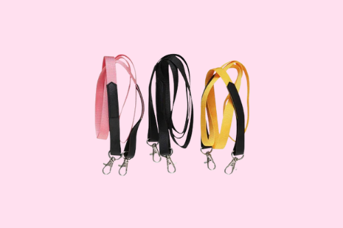 Drei bunte Schlüsselbänder mit Metallhaken in Pink, Schwarz und Gelb auf rosa Hintergrund.